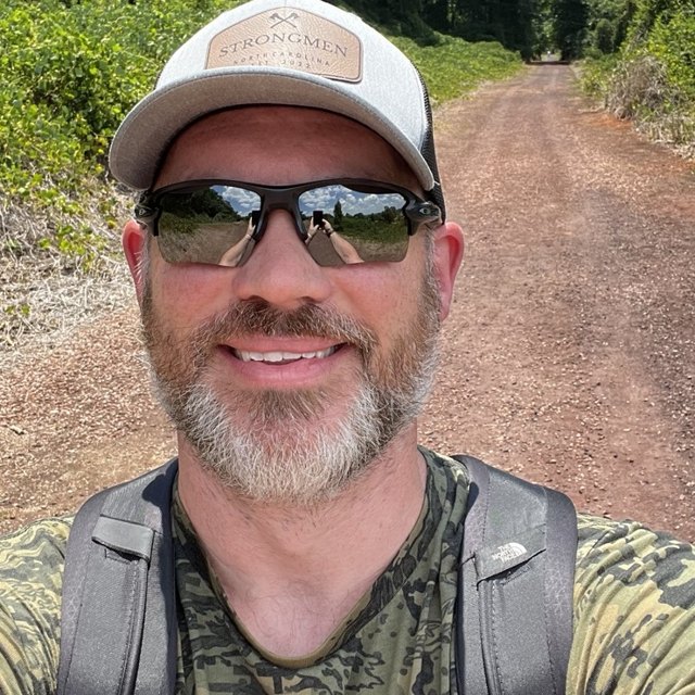 Ryan Puckett smiling on a wooded trail, wearing a StrongMen cap
